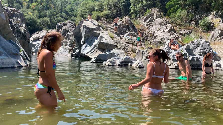 Amis rigolant les pieds dans l'eau au milieu de la rivière entourée par les rochers de granit